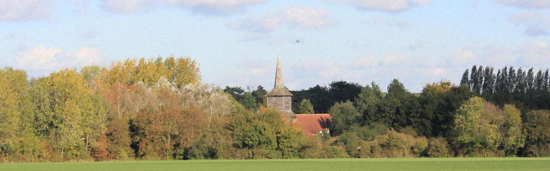 An autumn view across open farm land towards the bell tower of St Laurence church.