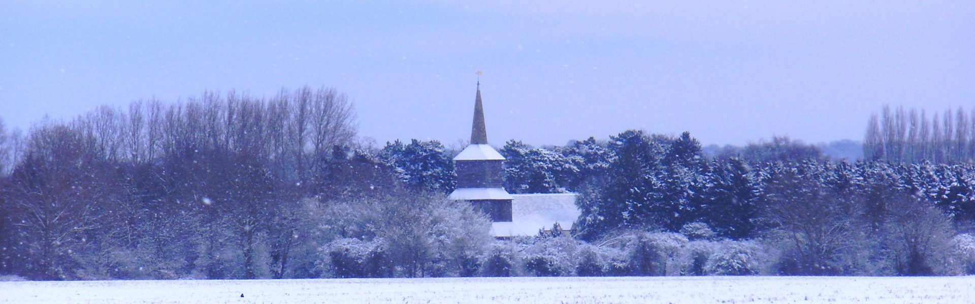 A snowy view across open farm land towards the bell tower of St Laurence church.